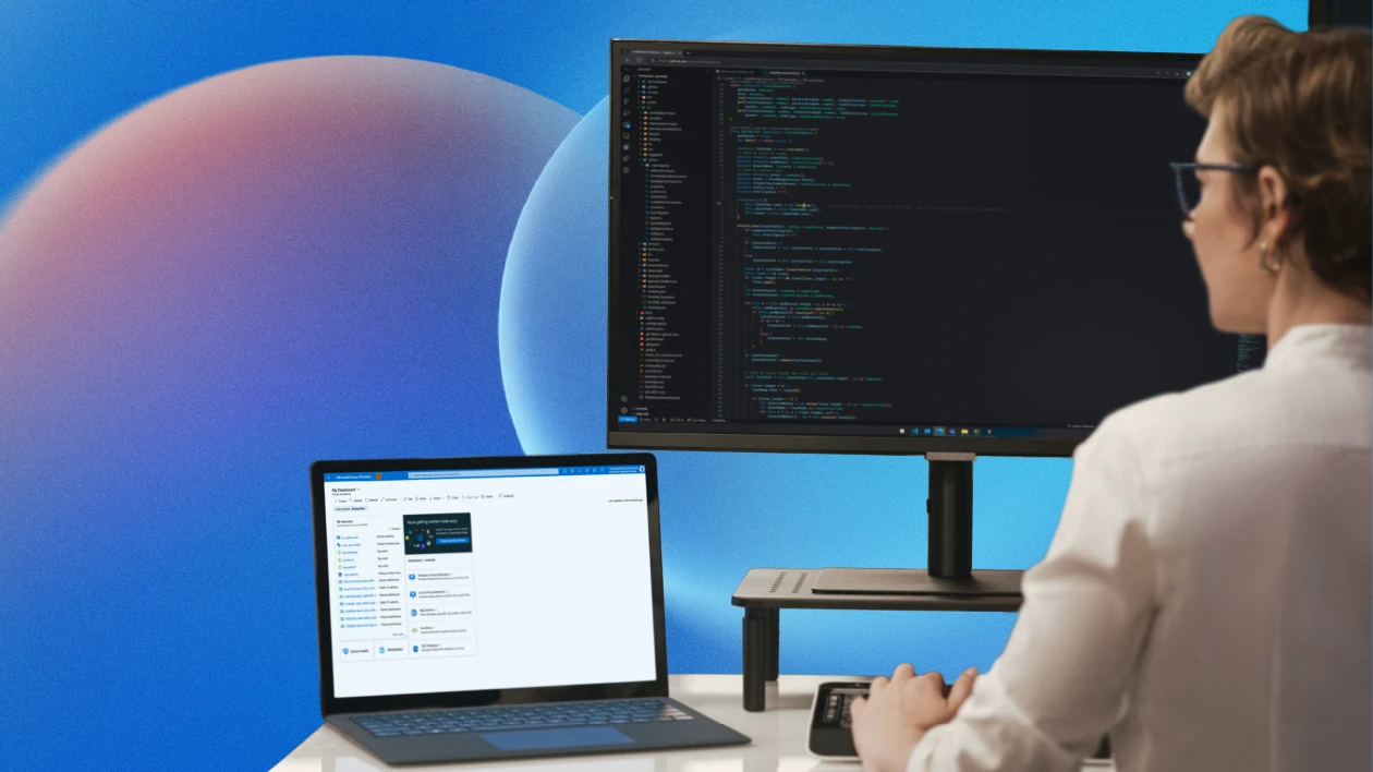 Person sitting at computer with one desktop monitor and one laptop with a blue background behind both