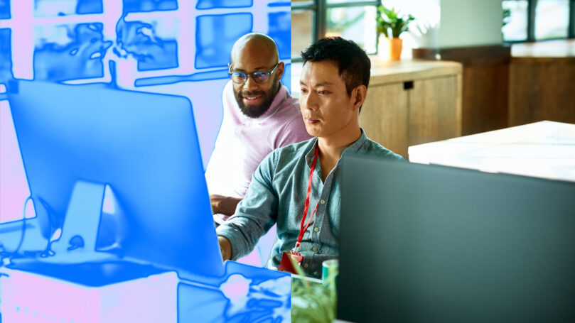 Two men sitting at a desk in front of computer monitor in an office setting with a blue overlay on the image.