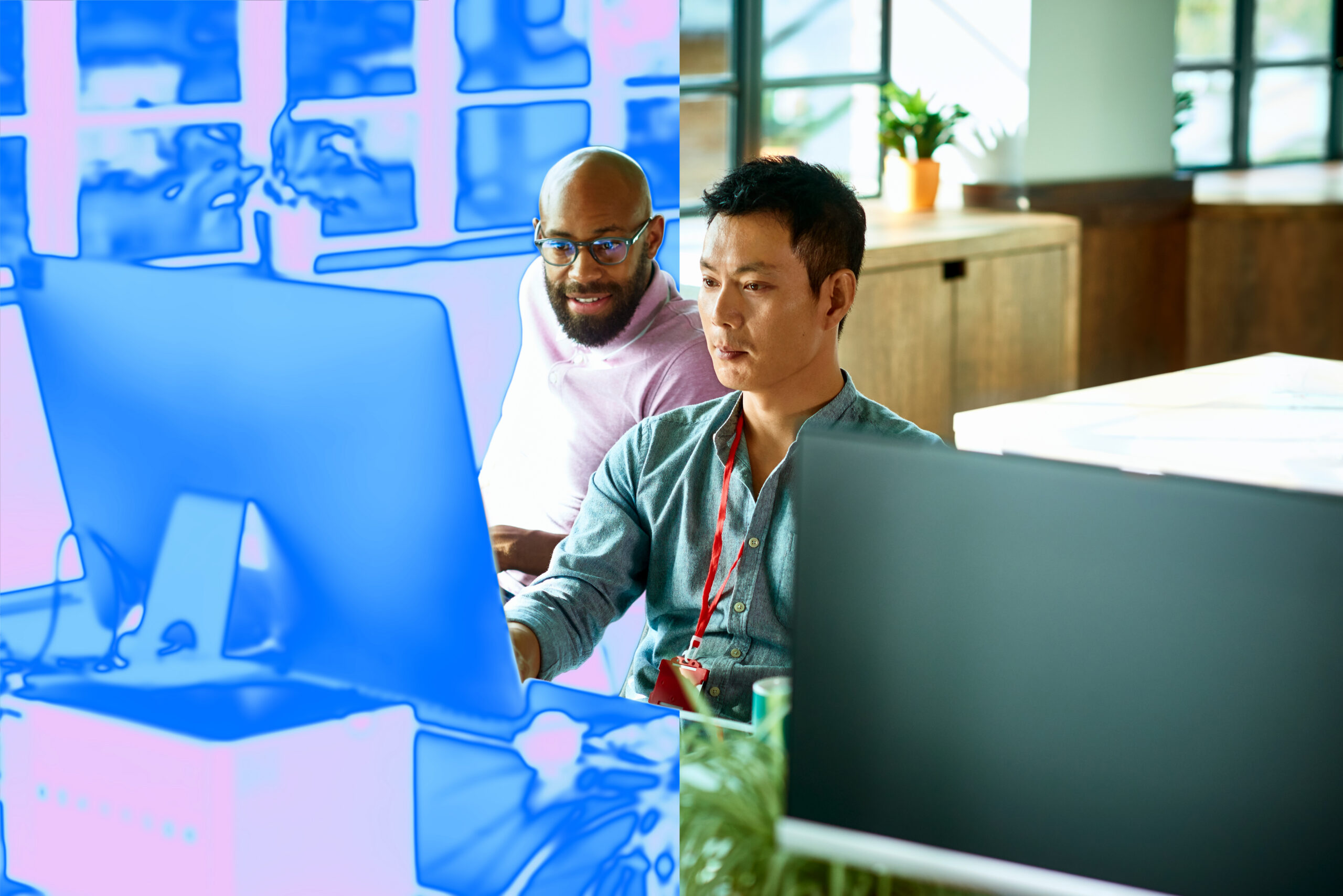 Two men sitting at a desk in front of computer monitor in an office setting with a blue overlay on the image.