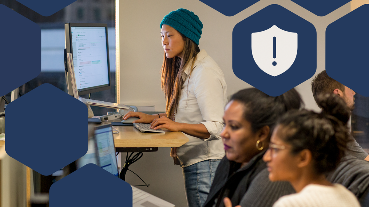 Female and male developers at work and collaborating. Some standing and some sitting using PC multi-monitor set ups.