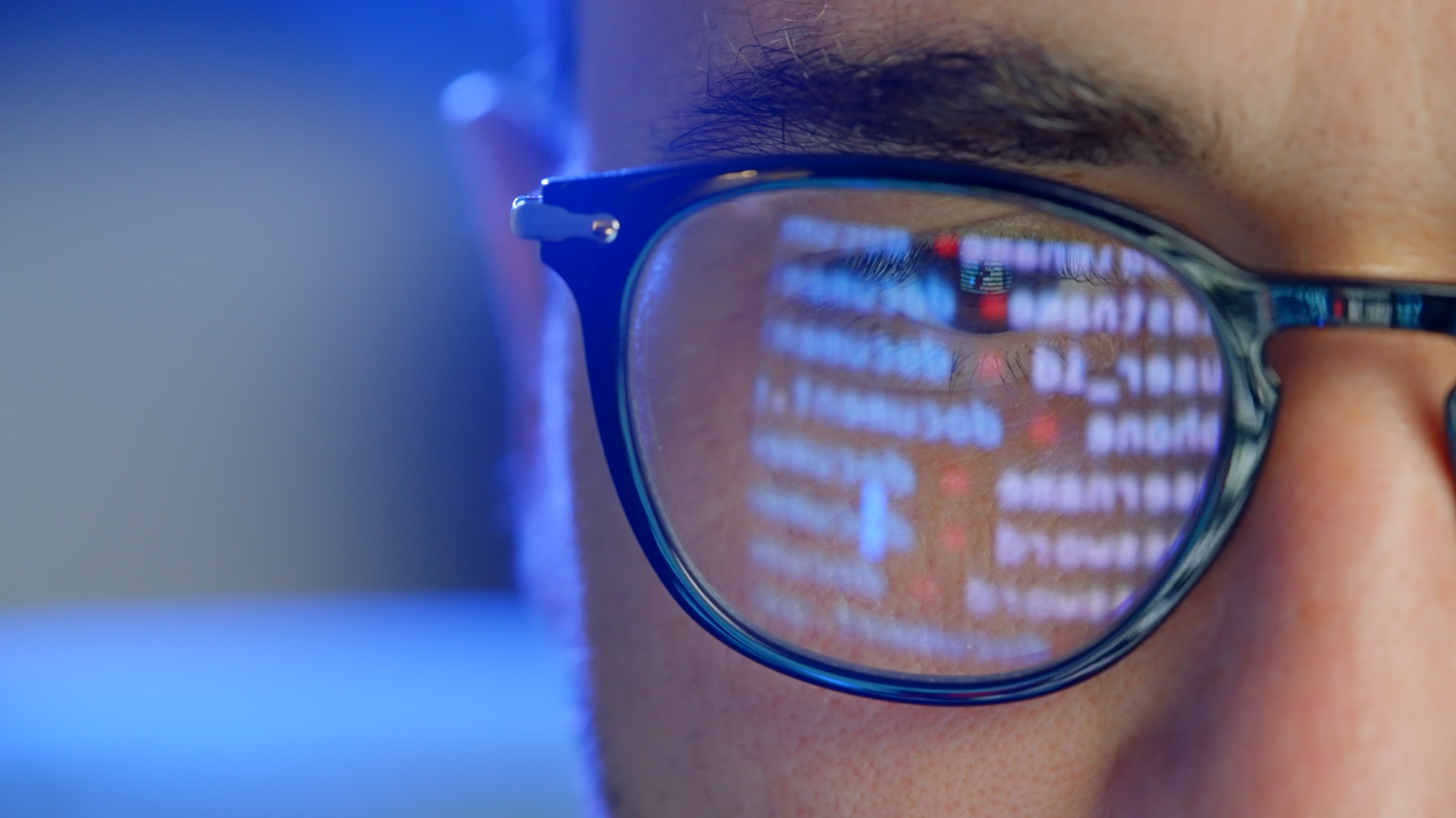 A person wearing glasses with code from a computer screen reflected in the lens.
