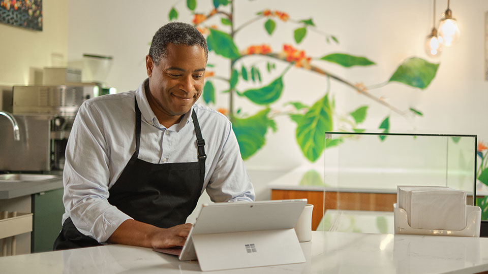 A man wearing an apron in a cafe uses a laptop