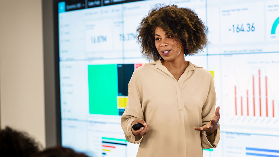 A woman presents in front of a large monitor