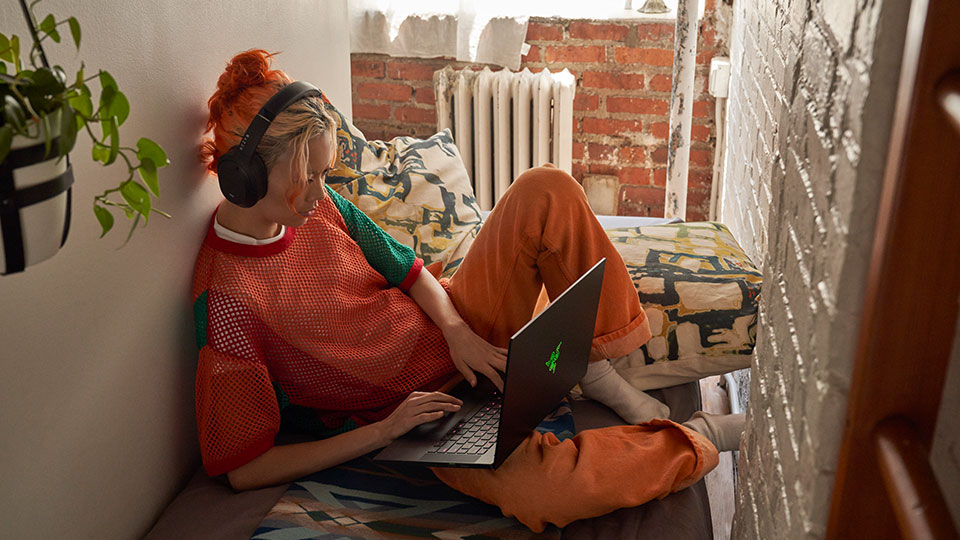 A woman wearing headphones reclines comfortably while working on a laptop