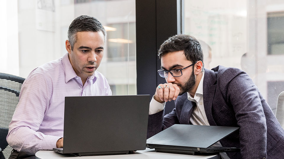 Two men discuss data displayed on a laptop screen