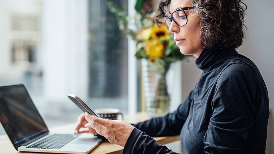 A woman sits with her laptop while checking her phone