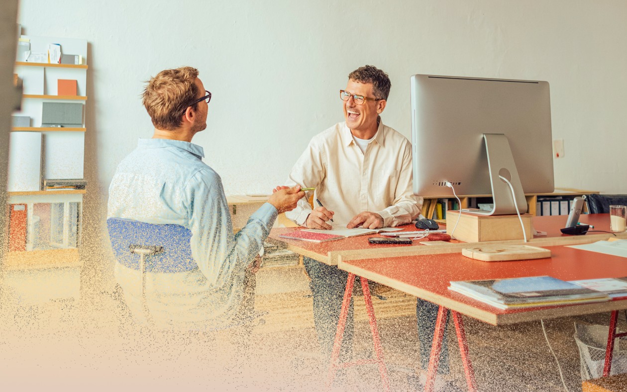 Two men sitting, talking and laughing in office.