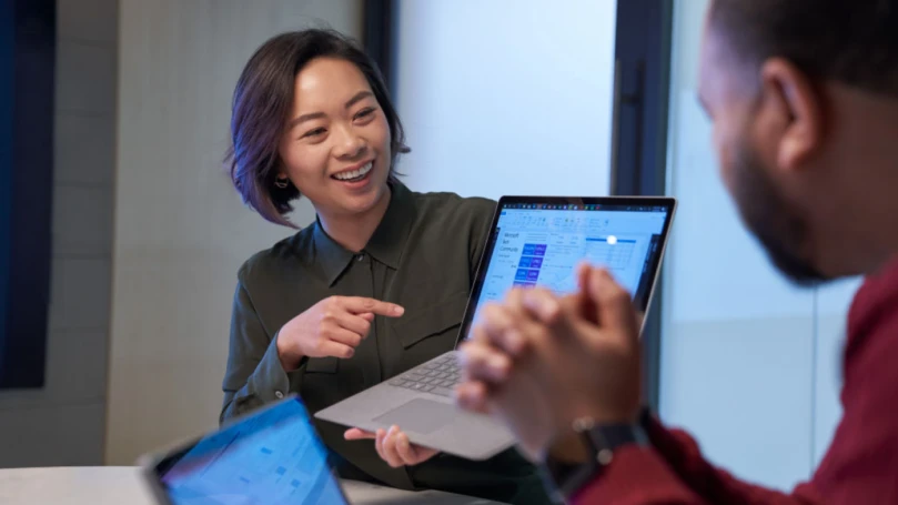 A woman shows a colleague a view of her computer screen.