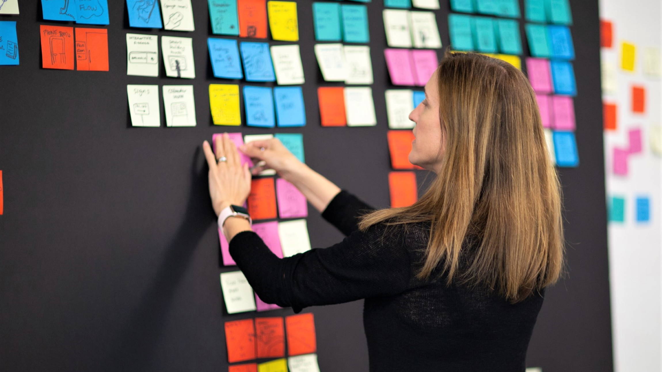 Tricia Fejfar writes on a sticky pad on a whiteboard covered with dozens of sticky pad notes.
