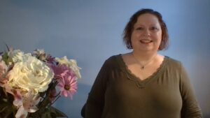 Kathren is standing in front of a vase of flowers, smiling in her home office.