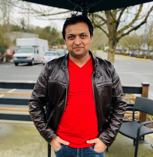 Karma stands on a back patio, hands tucked into his pant pockets.