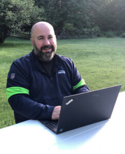 Gagnon sits at a table with his laptop and smiles for the camera.