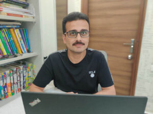 Mahajan sits at his desk, a bookshelf to his left.