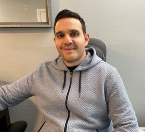 Mango sits at his desk and smiles at the camera.