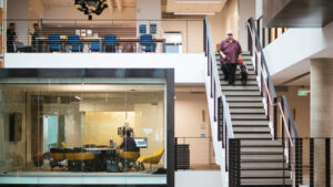 The interior of a Microsoft building showing a person walking down stairs and an office area.