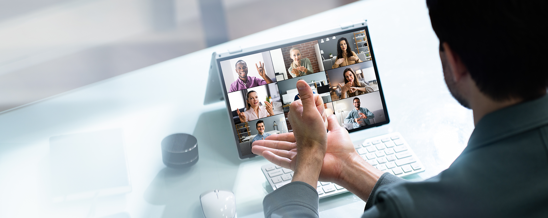 ノートパソコンでバーチャルミーティングに参加している人、画面上に複数の参加者が手話を使っているのが見える。