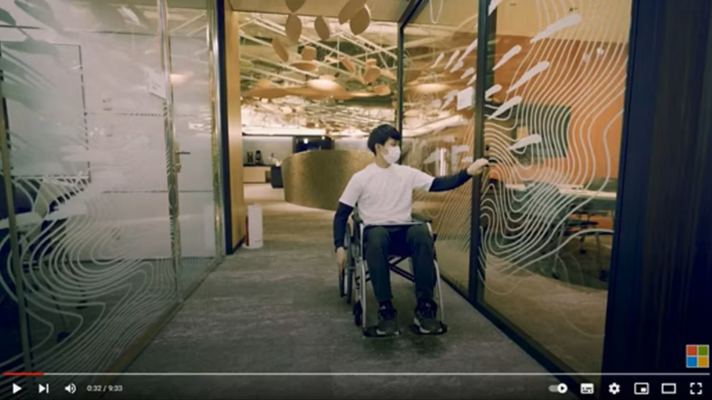 YouTubeの一場面。車いすの男性が会議室の大きな扉を片手で開けようとしている