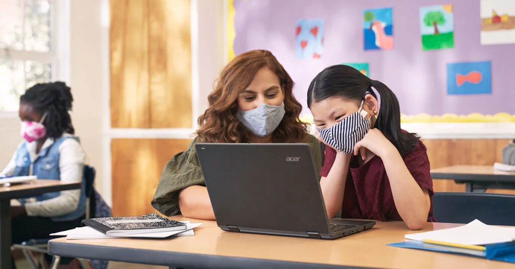 教室でパソコンを使用する生徒と先生の写真