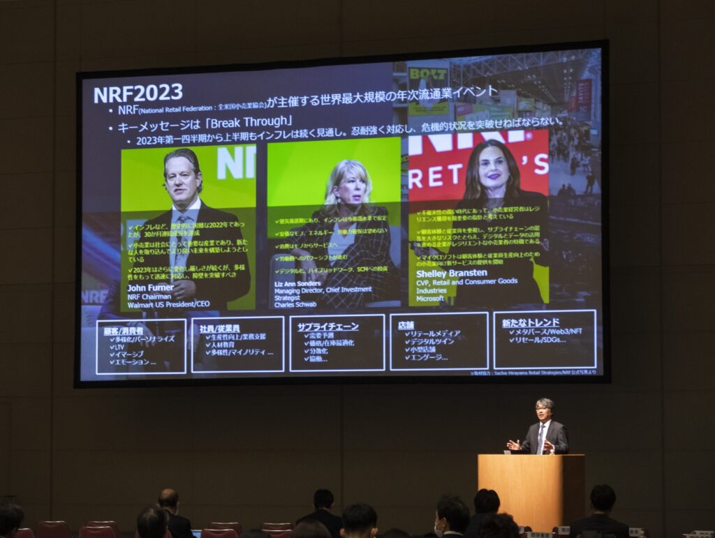 壇上で大型スクリーンを前に男性が講演する様子