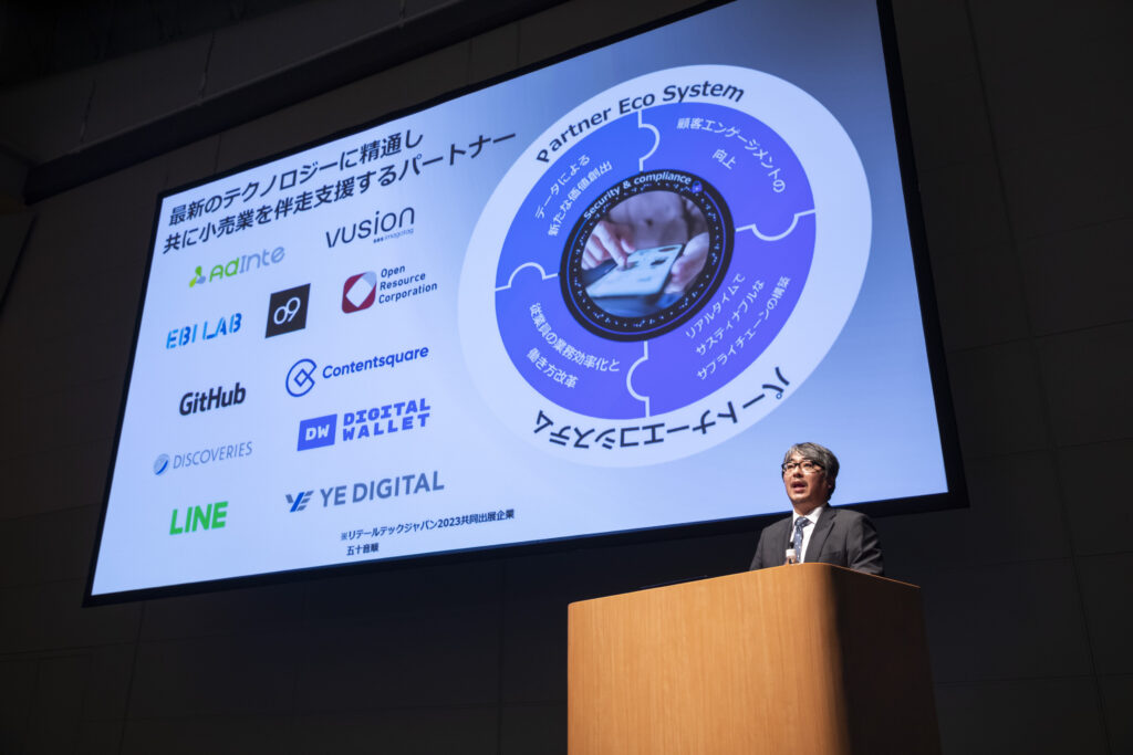 壇上にて大型スクリーンを前に講演を行う男性