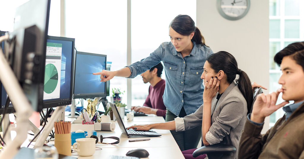 オフィスで同僚社員にモニターを指さしながら何かを伝える女性