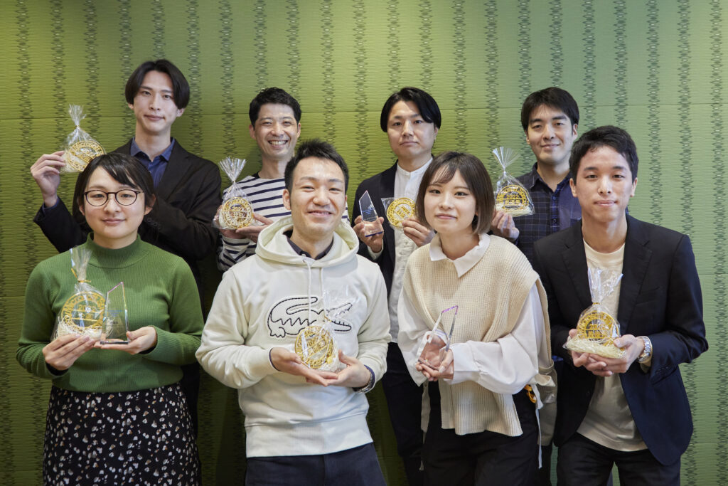 表彰盾を手に、上下 2 列に並ぶ授賞チームのメンバー