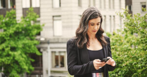 市庁舎の背に立ちスマートフォンを操作する女性