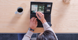 コーヒーが置かれたデスクの上で PC を操作する男性を上から見た様子