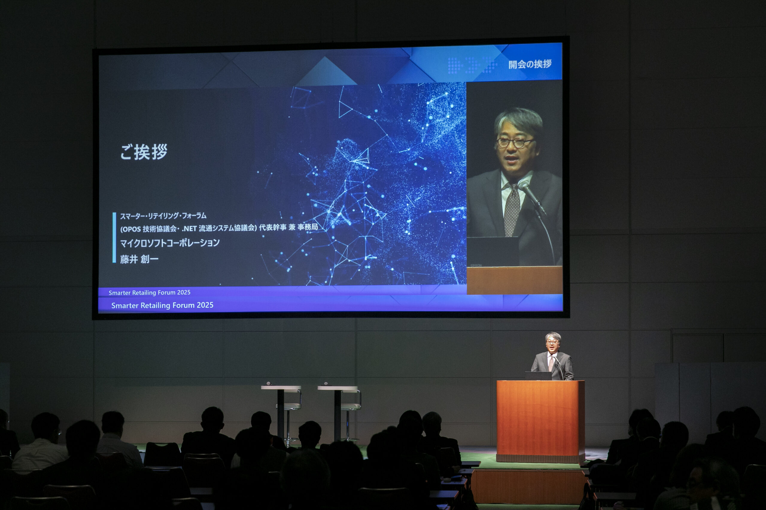 A man standing at a podium with a screen on the wall
