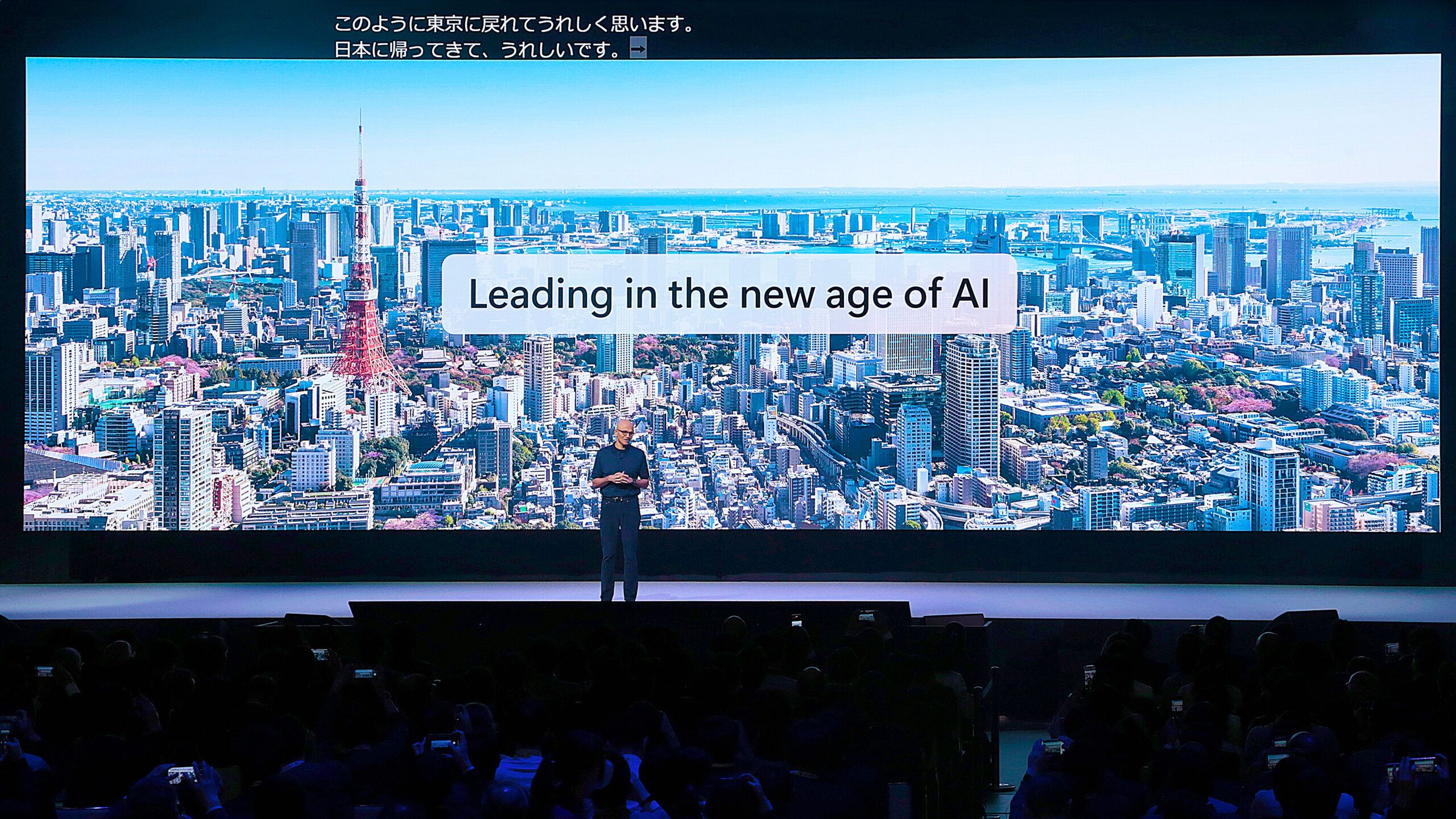 A man standing on a stage with a large screen with a city in the background