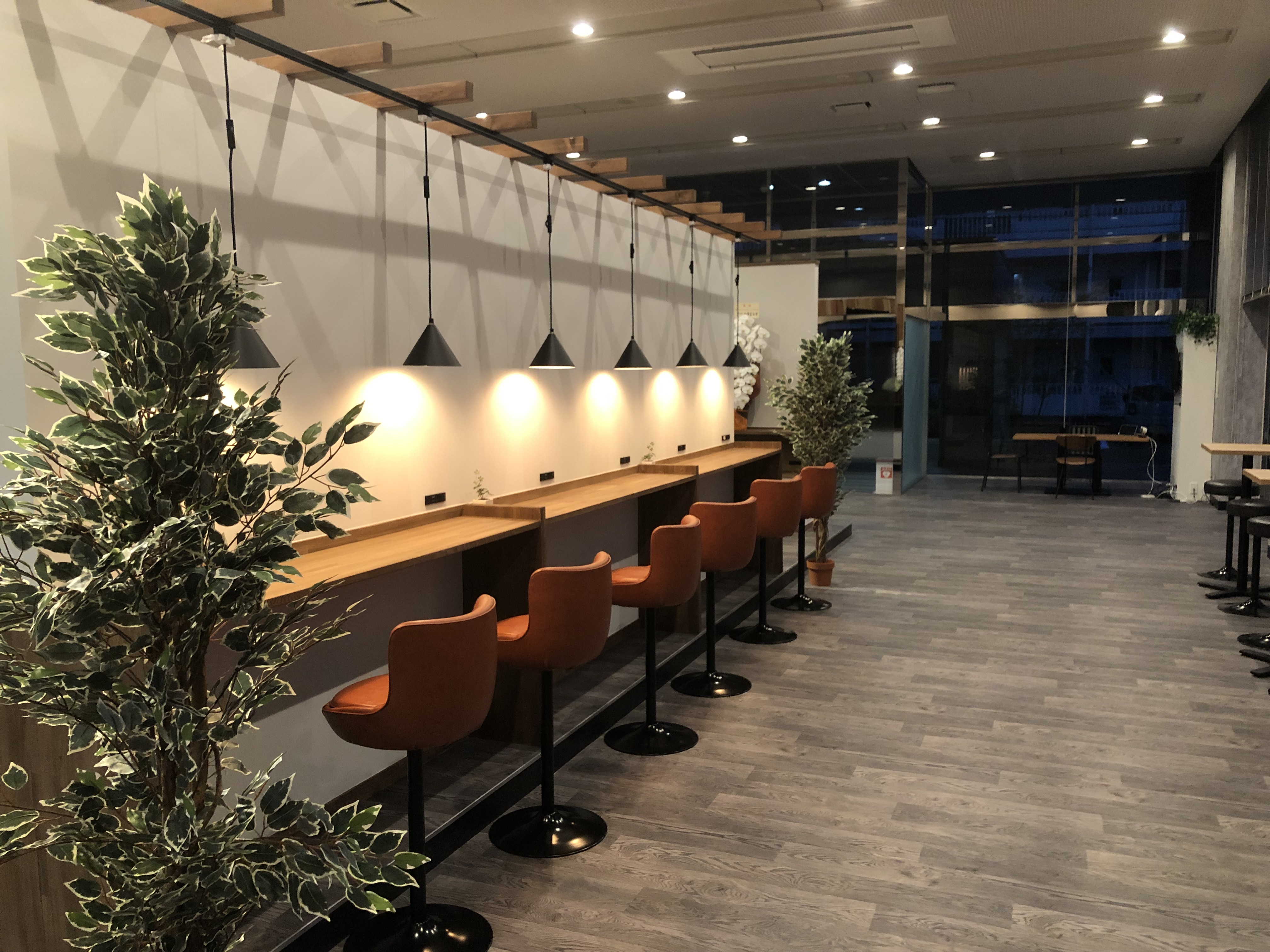 ペンダントライトとレザースツールが並ぶロングカウンターのくつろぎ型コワーキングスペース。