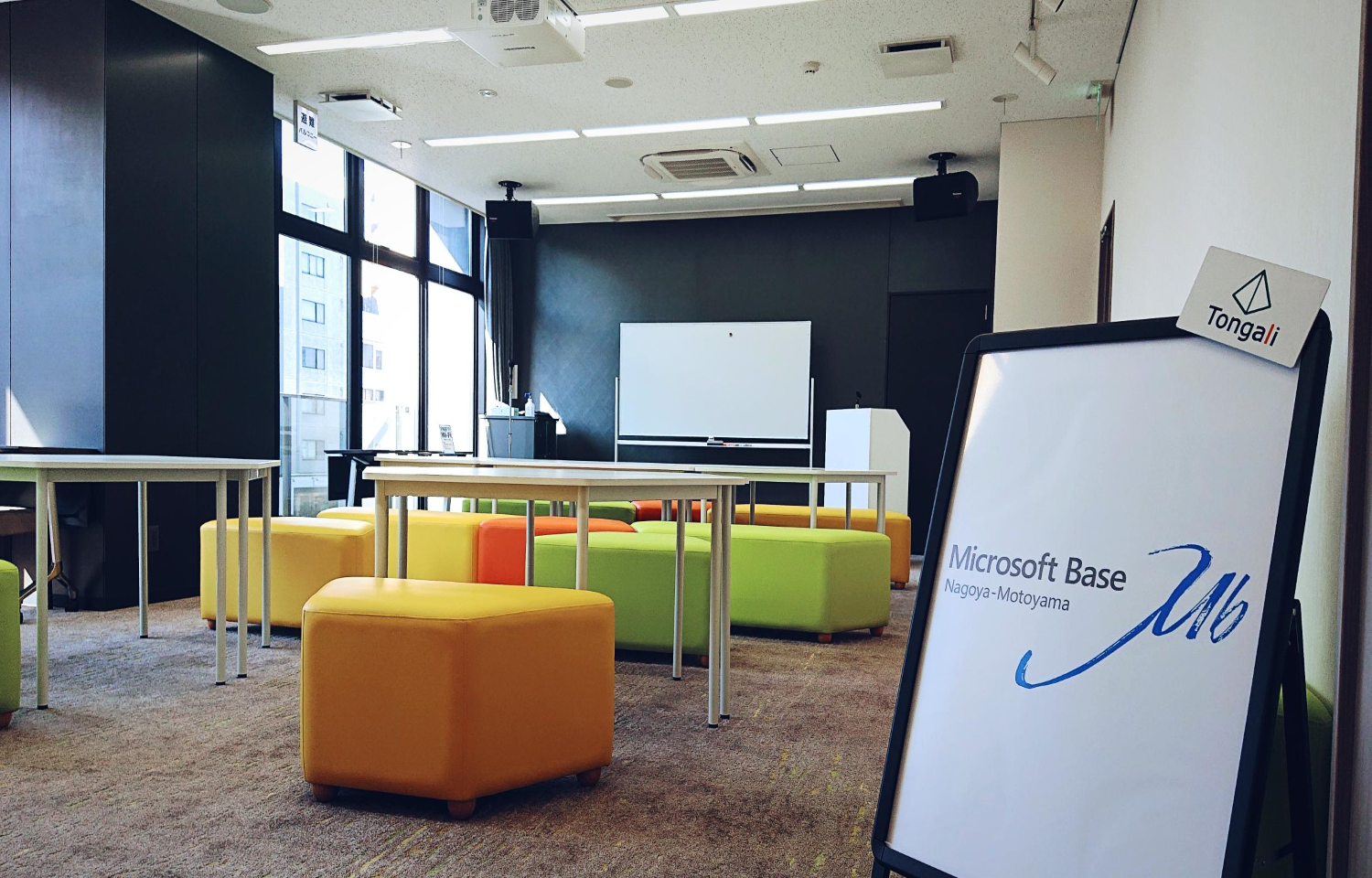 カラフルなオットマンとテーブル、立て看板がある多用途の会議スペース（「Microsoft Base Nagoya-Motoyama」）Tongali。