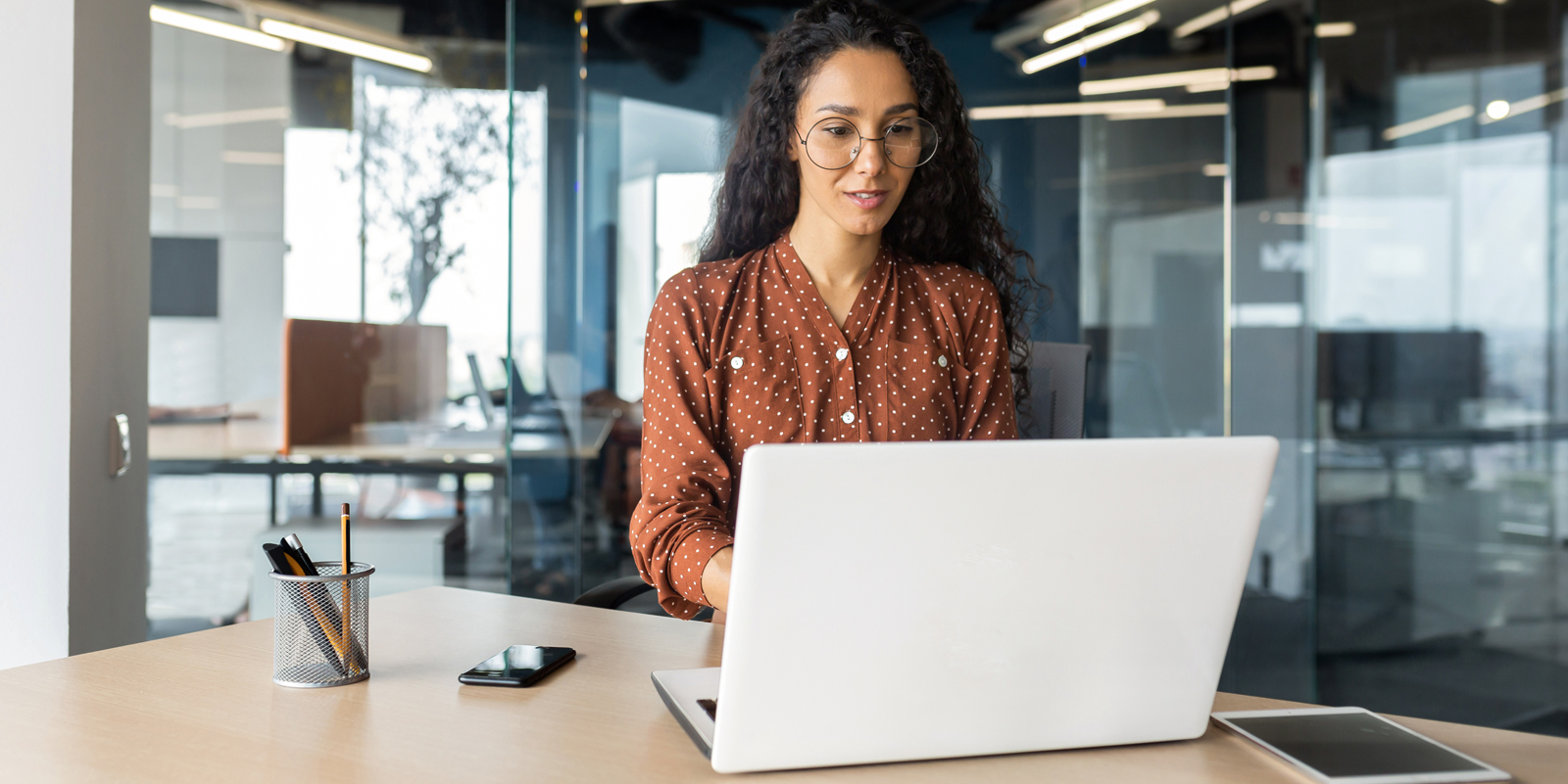 Uma mulher em uma sala de reunião de vidro utilizando um notebook.
