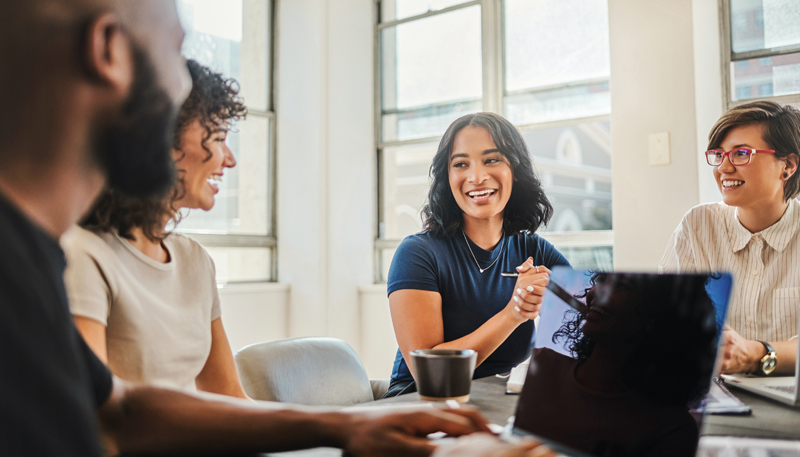 dois homens e duas mulheres sentados em uma sala de reunião rindo com notebooks na mesa.
