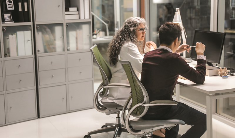 Uma mulher e um homem sentados a mesa olhando para um monitor em um laboratório