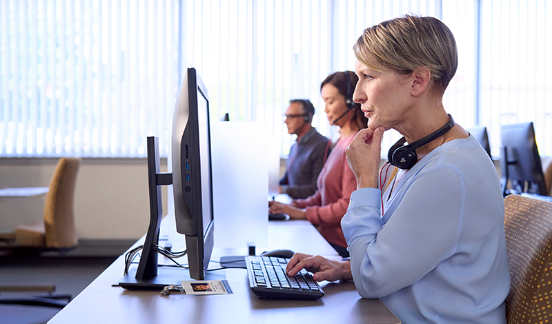 Os representantes de atendimento ao cliente trabalham em seus computadores, usando fones de ouvido.