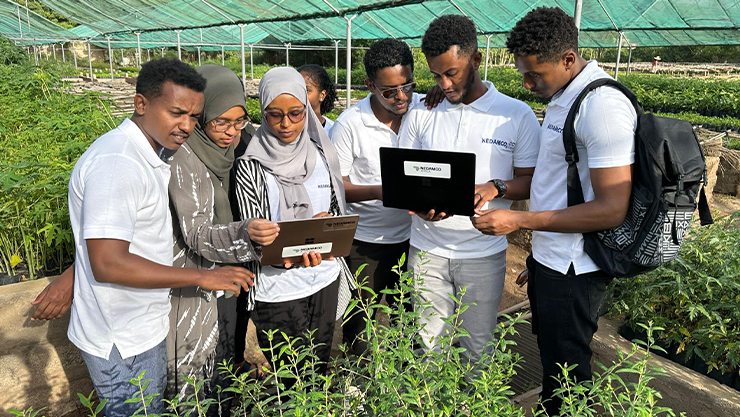 a group of 7 people in agriculture farm while holding laptops